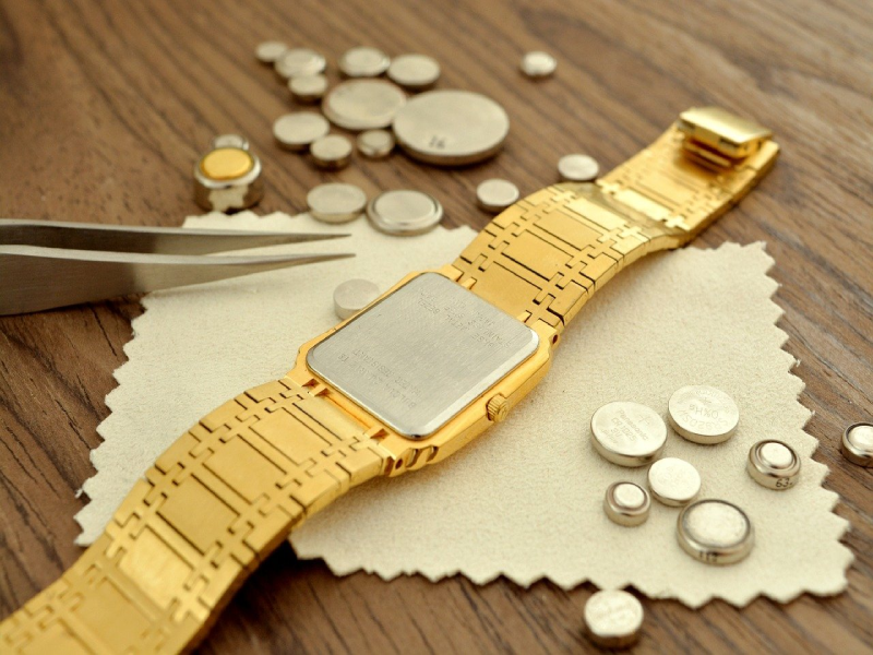 gold watch upside down surrounded by watch batteries